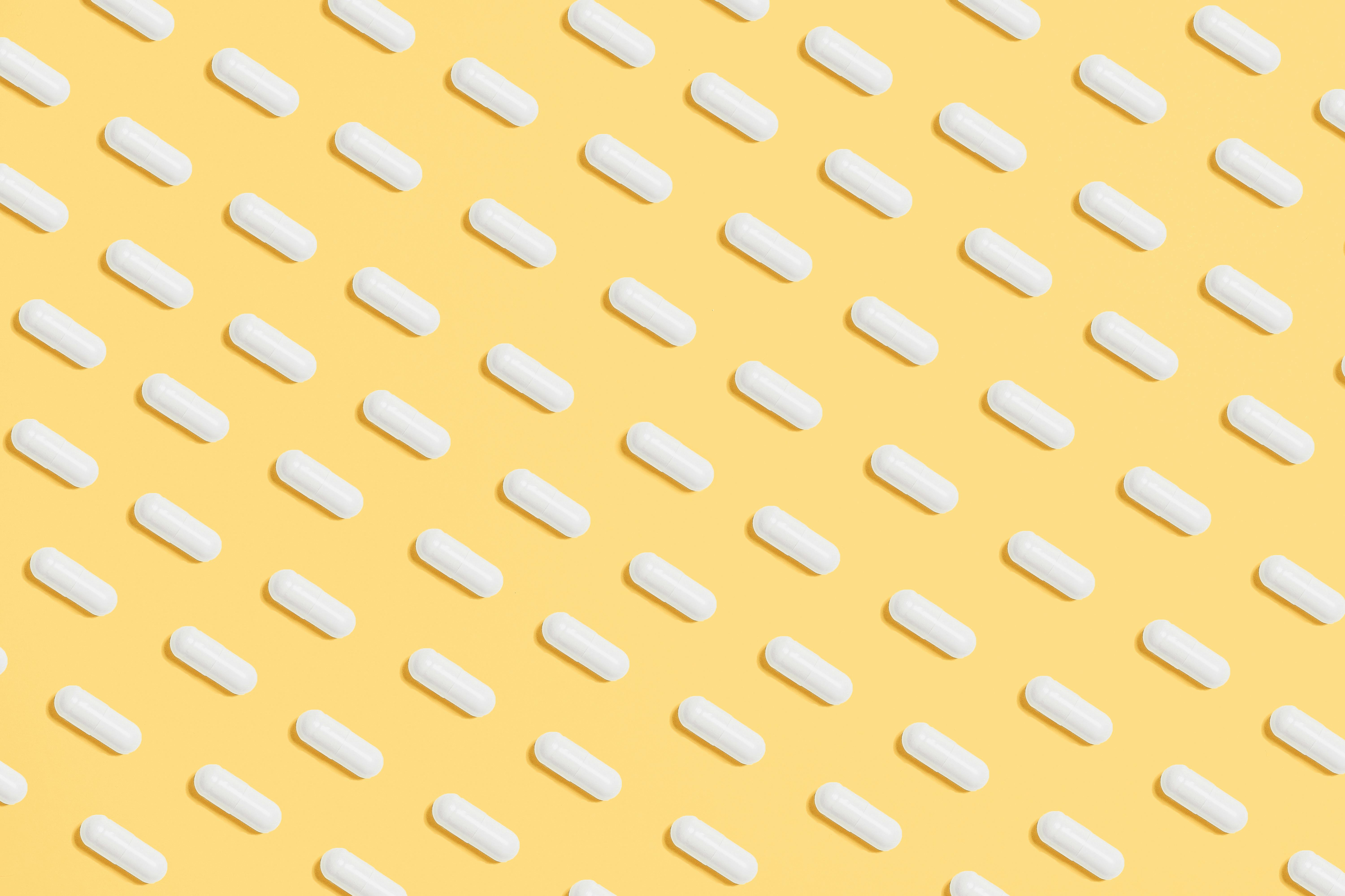 Pattern of white capsules on a bright yellow surface, symbolizing healthcare and medicine.