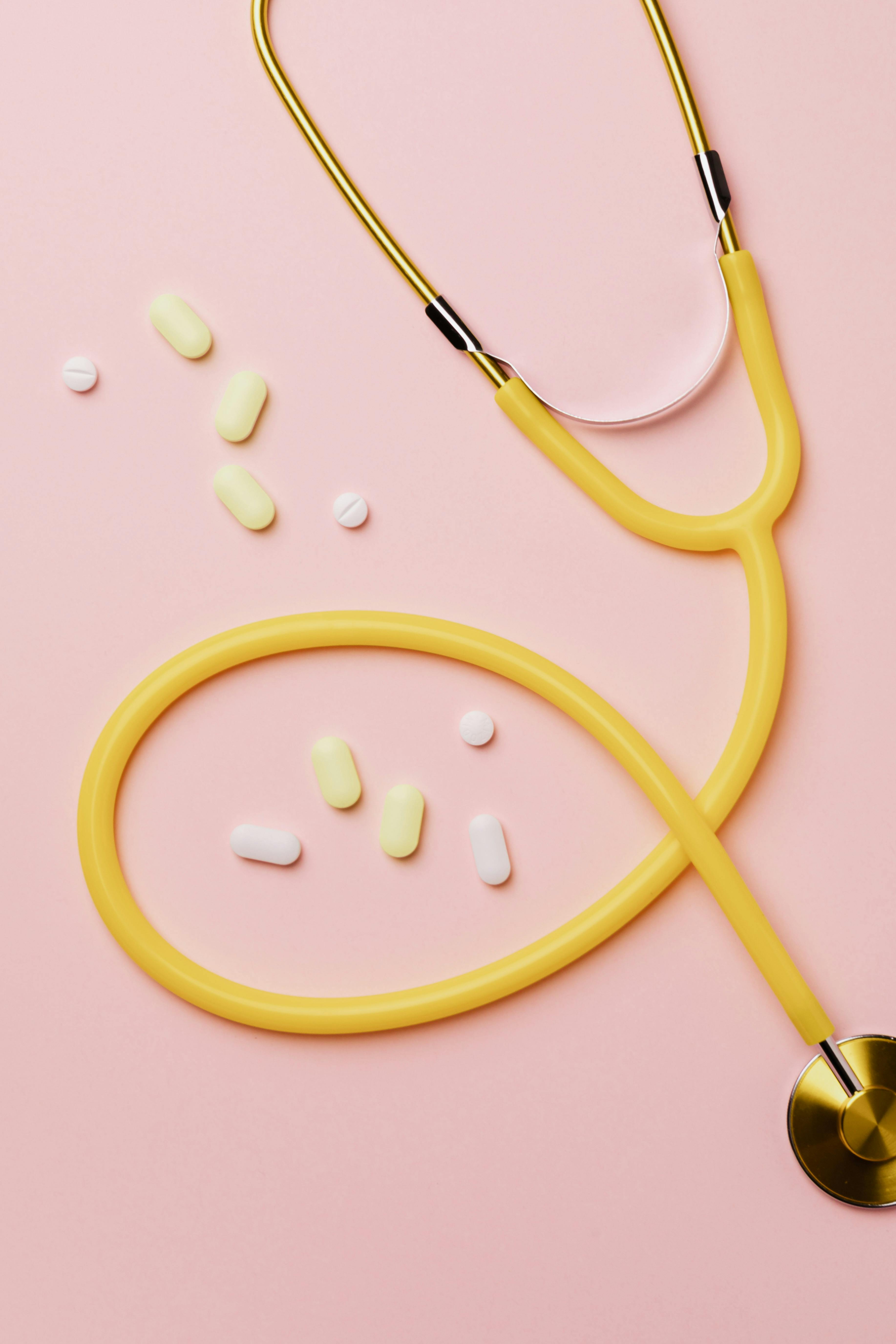 Yellow stethoscope with pills on pink background symbolizing healthcare and diagnosis.